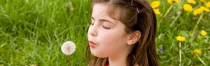 a girl in a meadow is blowing a dandelion