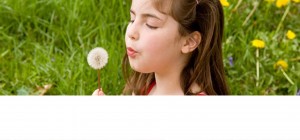 a girl in a meadow is blowing a dandelion