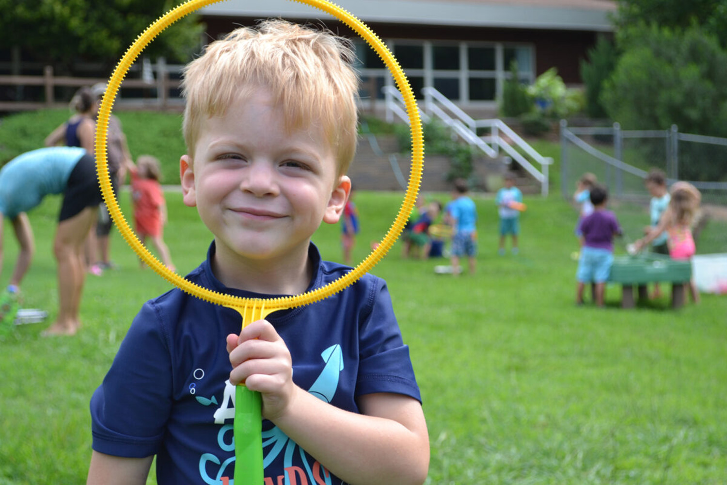 boy looking through large yellow bubble maker wand at The New School spring picnic